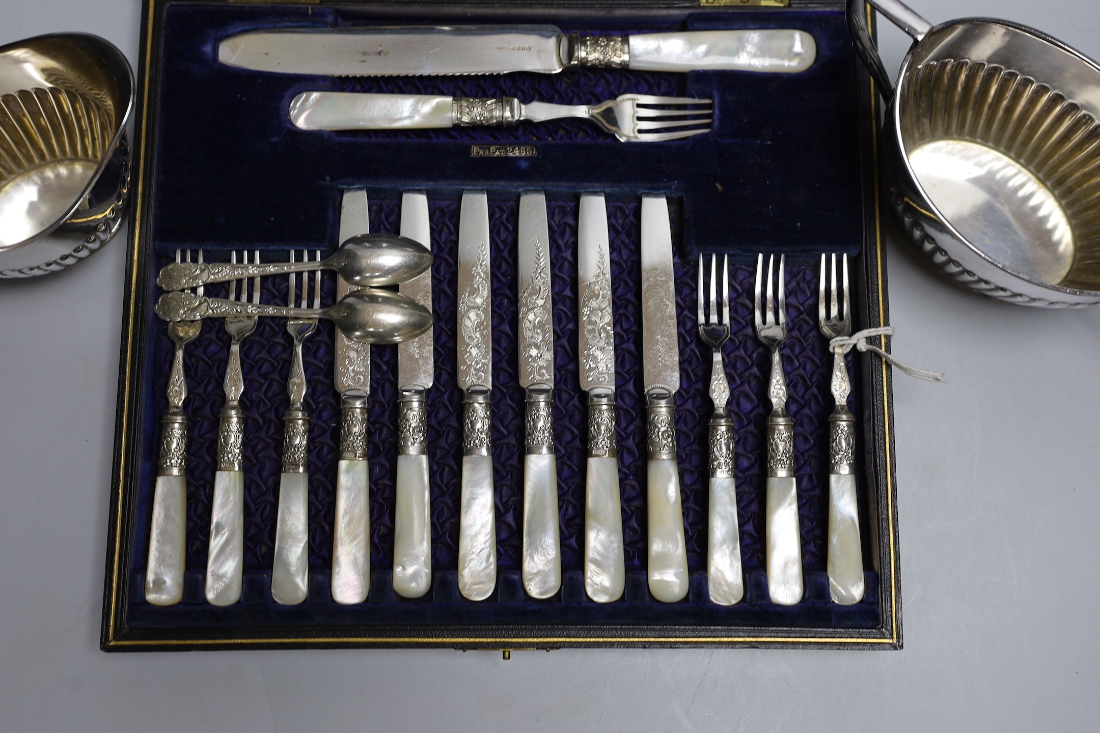 Six pairs of silver plated and engraved dessert knives and forks, with server, mother of pearl handles and six teaspoons (cased) and a silver plated cream jug and sugar bowl.